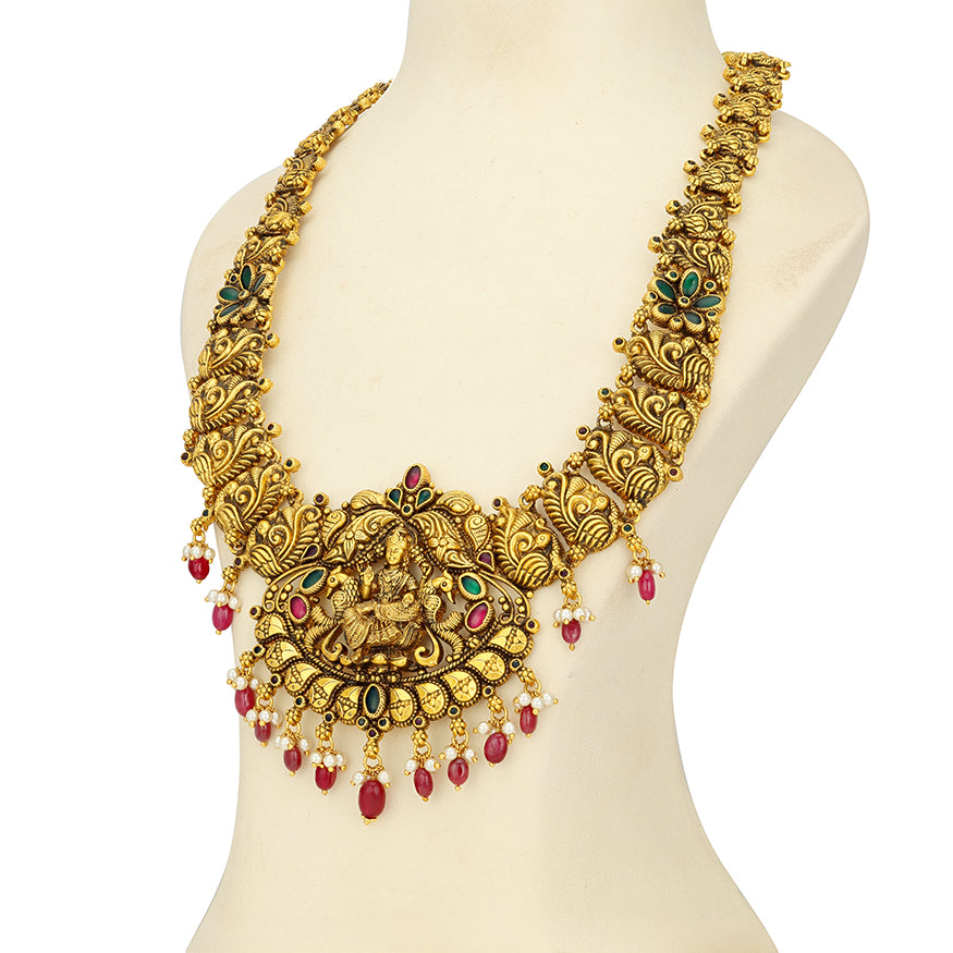 Gold necklace with intricate designs and red beads on a mannequin