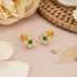 Gold earrings with green gemstones on a pink surface with flowers and leaves.